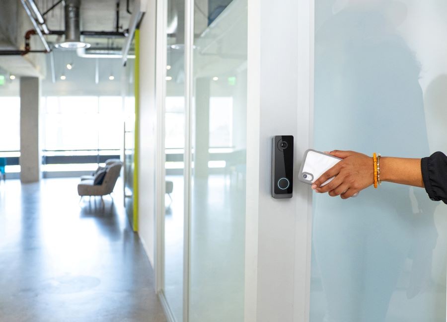 A person’s hand holding a smartphone in front of an access control reader.