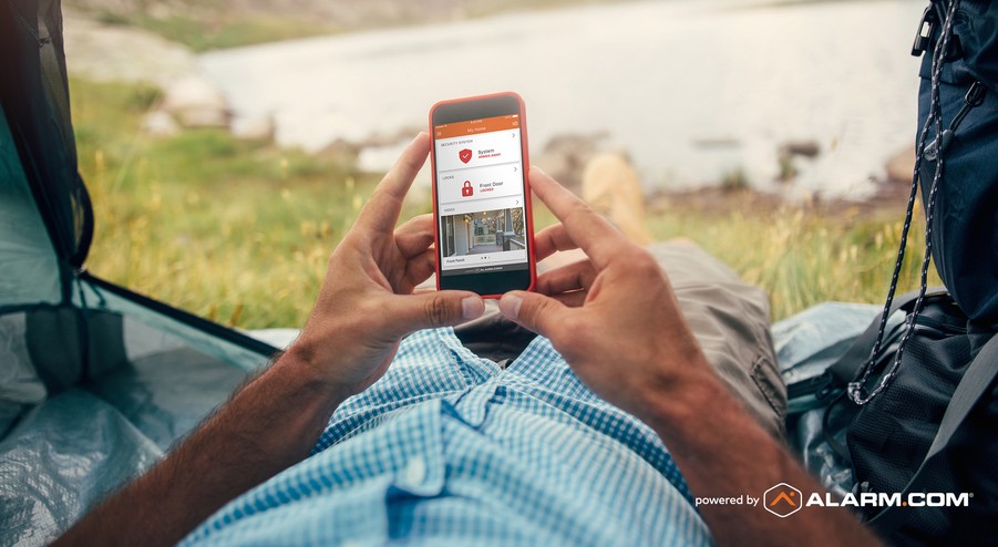 A person relaxing in nature holding a smartphone showing the status of their home security system in Springfield, MO.